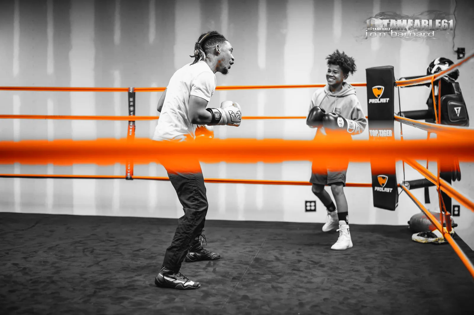 Coach and young boxer squaring up in the ring behind orange ropes